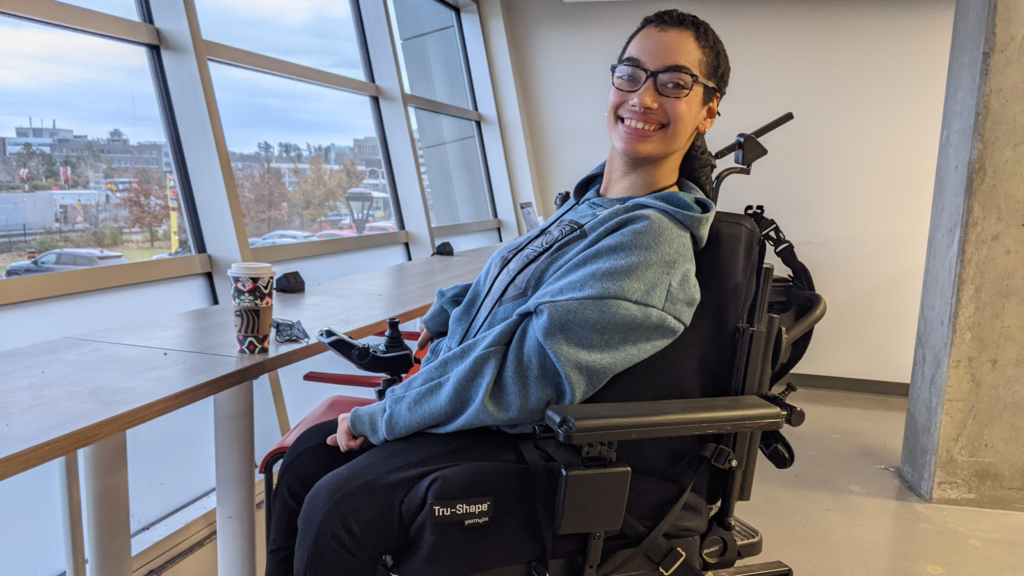Jay Baldwin at Carleton University smiling in their raised wheelchair