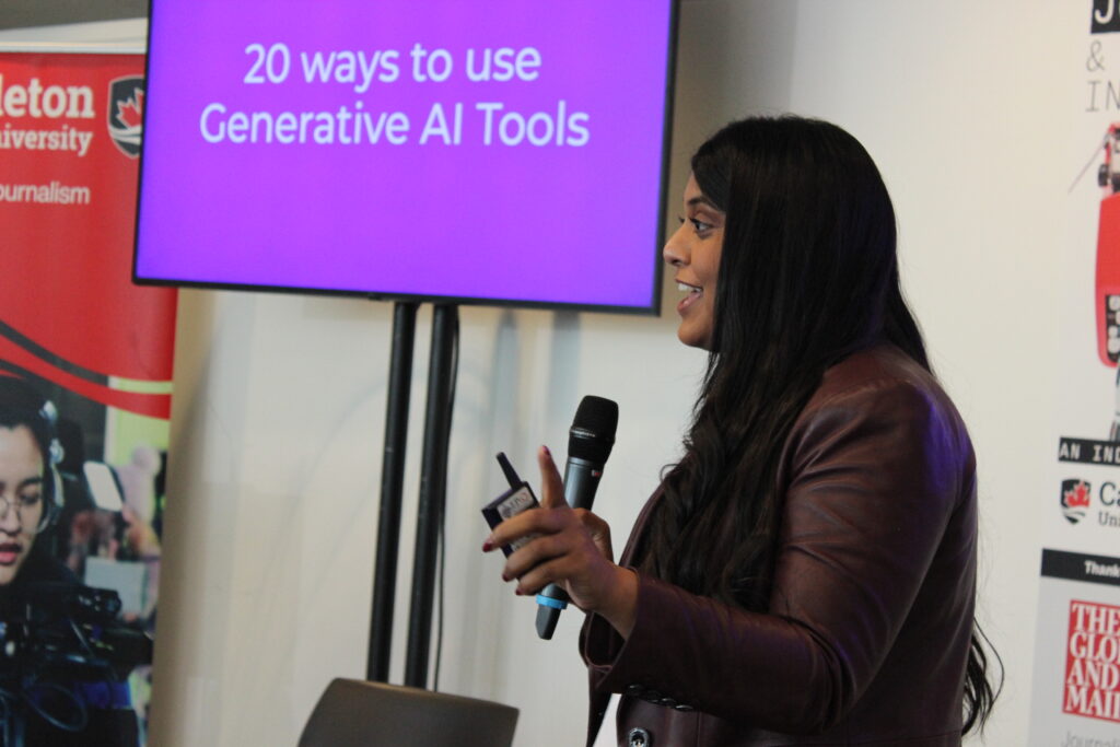 Nikita Roy speaking at ournalism and Artificial Intelligence: An Industry Roundtable. She is standing with a microphone in her hand with a screen behind her that says, "20 ways to use Generative AI Tools."