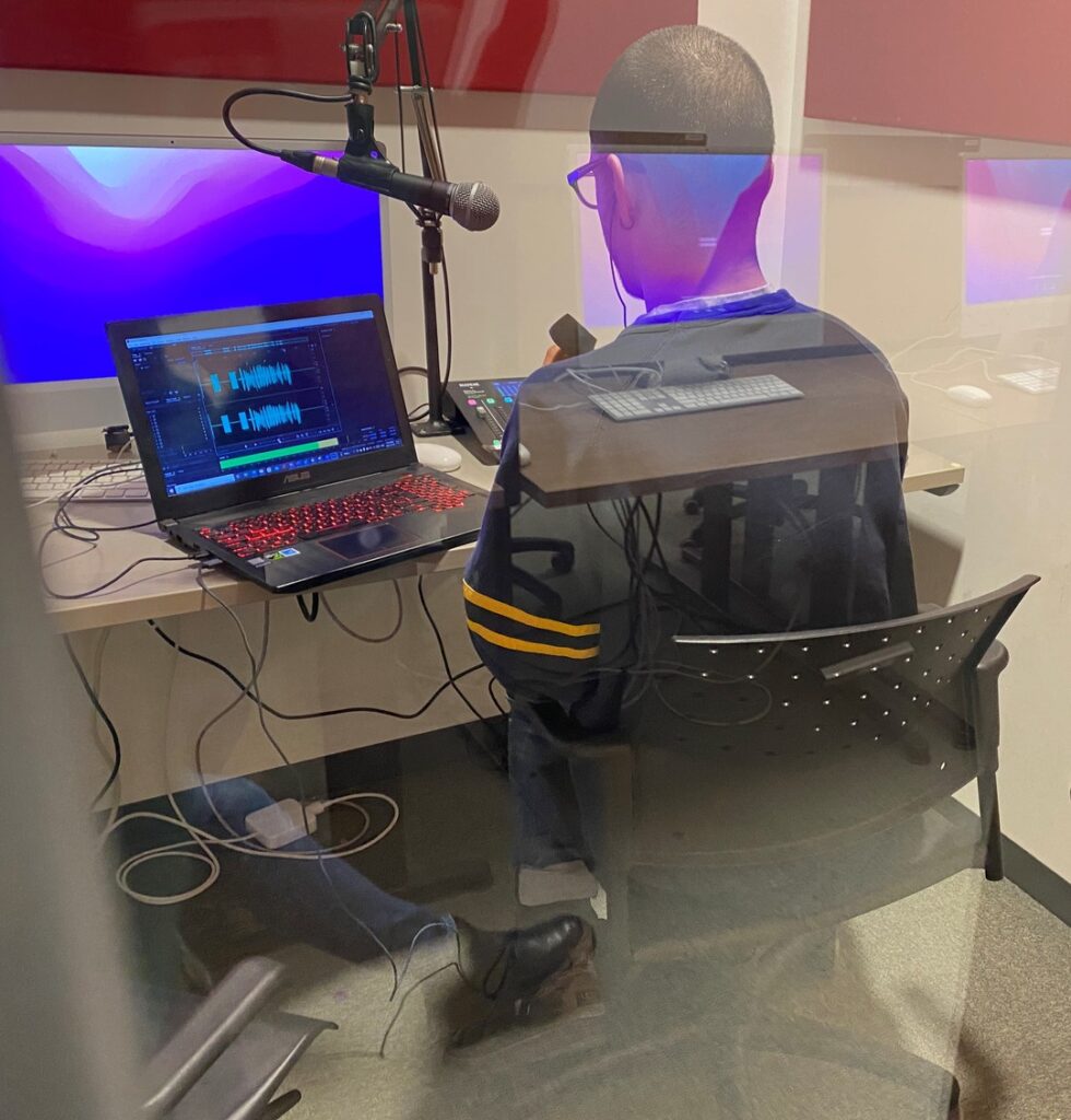reporter works in glass booth, looking ghostly due to reflections