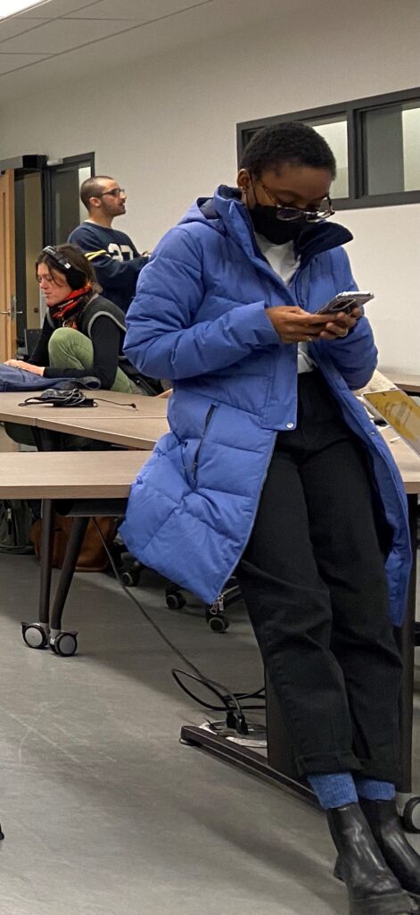 Reporter in mast and long down parka checks her phone in the newsroom