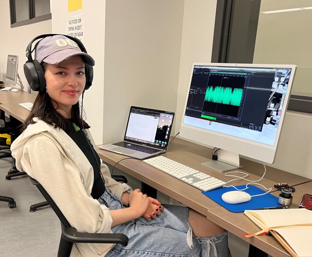 audio producer in headphones with wave pattern of sound file on her computer screen
