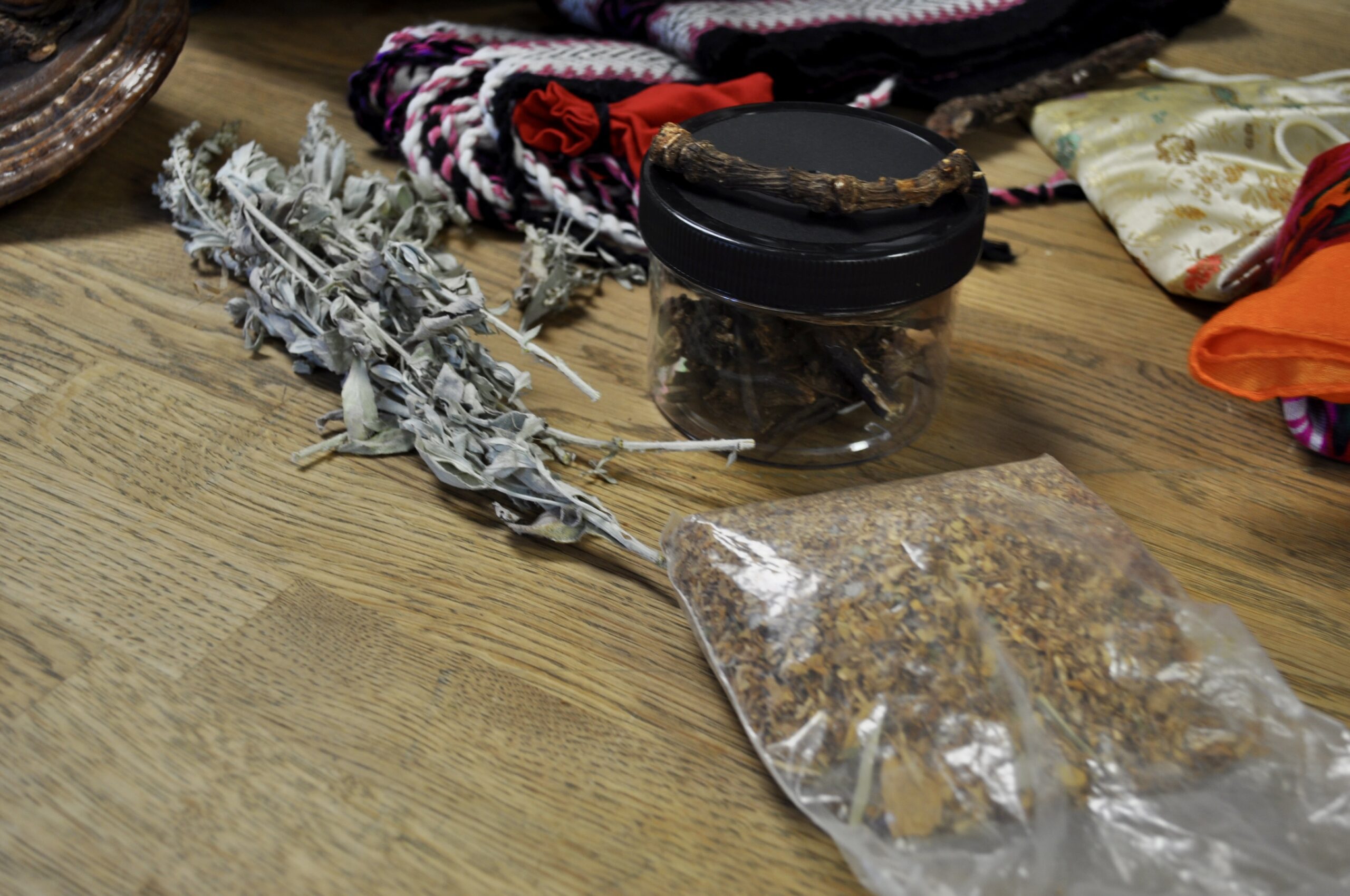 A collection of medicines provided by Kalyn Kodiak including a jar of bear root, white sage and a bag of tobacco.