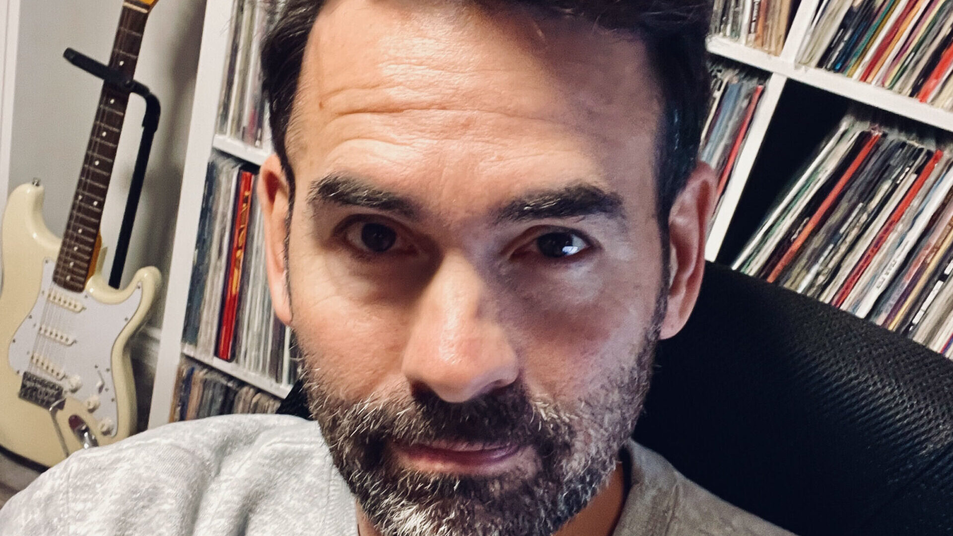 Josh Greenberg sitting in front of a large shelf containing his record collection.