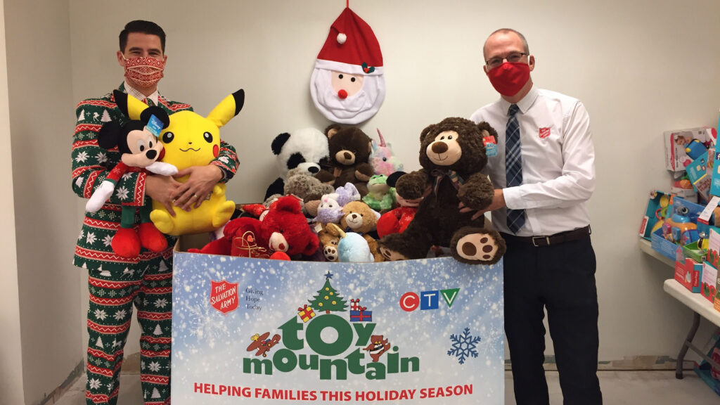 Two men stand next to a cardboard bin full of stuffed animals.