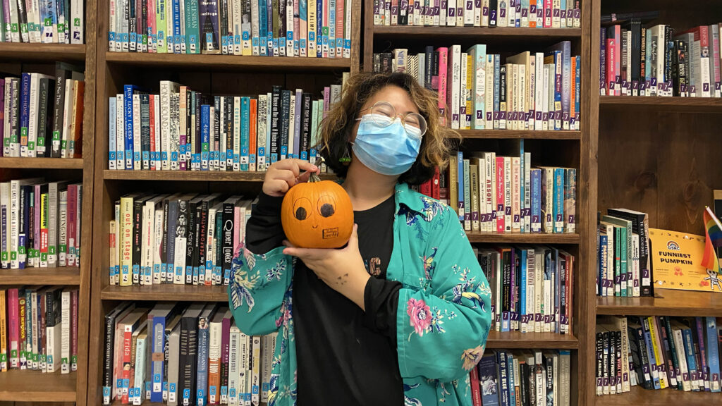 Gabbie Cruz holds a pumpkin in front of a bookcase 