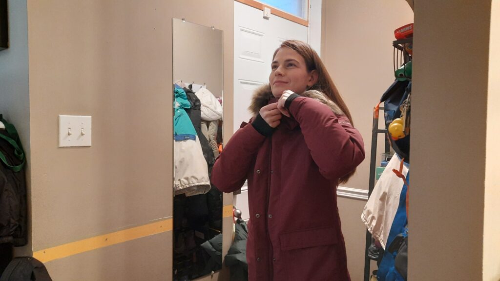 A woman is zipping up her red jacket next to a mirror.