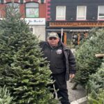 A business co-owner standing with Fraser Fir Christmas trees.