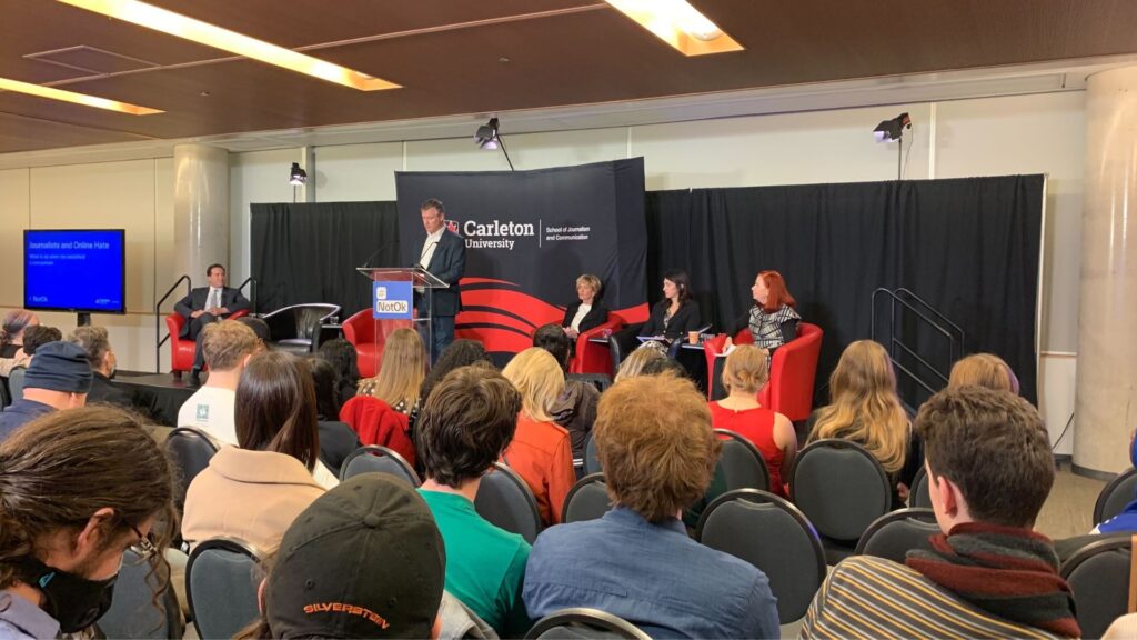 Allan Thompson stands at the centre of the stage in front of attendees of the event.