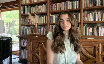 Sarah Cupello sitting at a table in front of a bookshelf full of books.