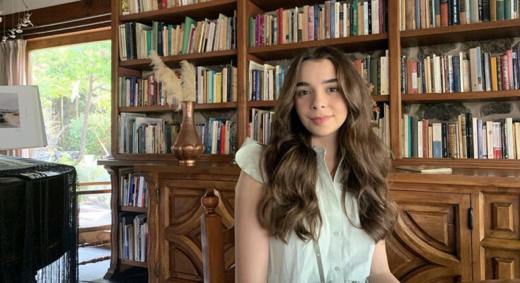 Sarah Cupello sitting at a table in front of a bookshelf full of books.