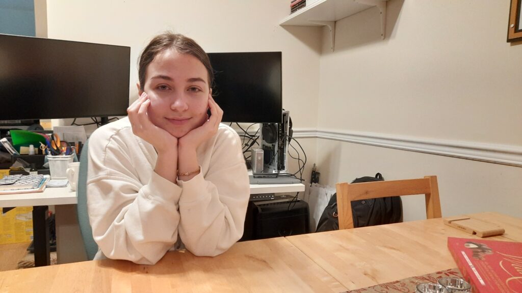 A woman in white hoodie is sitting at the table holding her head with her hands.