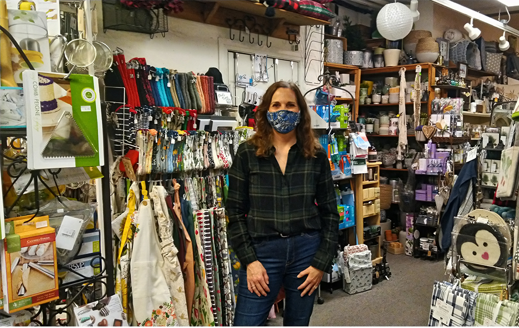 Jennifer Adam smiles behind her mask while standing in front of the various kitchen and home products inside J.D. Adam.