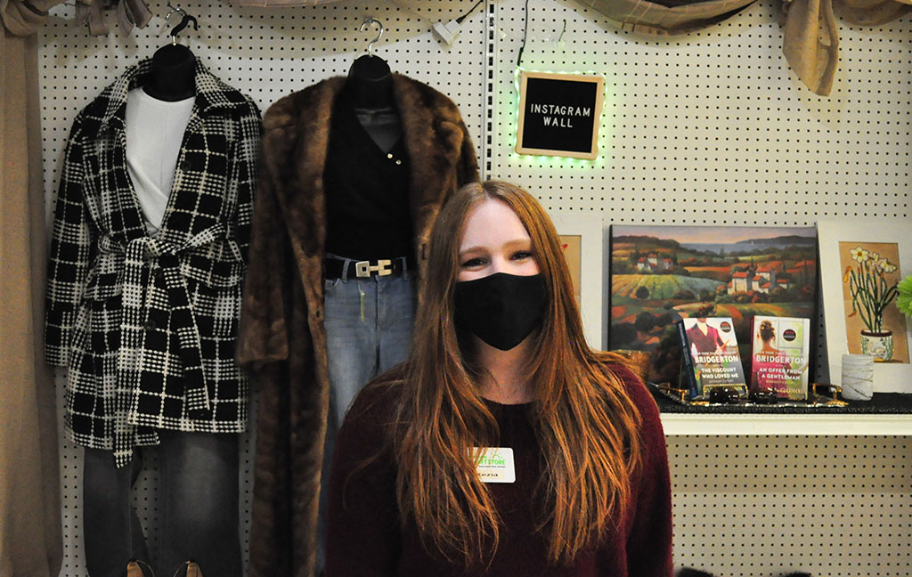 a young girl in front of a wall of fashionable clothes and books with a sign that reads "Instagram Wall"