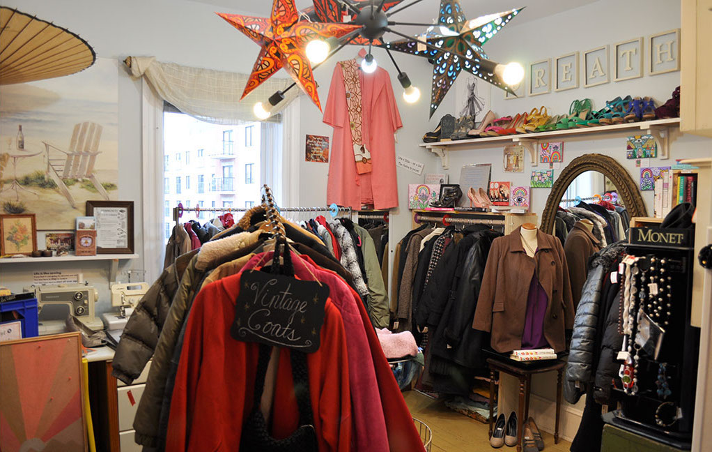 a room filled with beautiful thrifted clothes, a sign labeled "vintage coats" hangs on the front rack