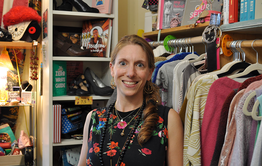 a young woman stands in front of a rack of beautiful thrifted clothes